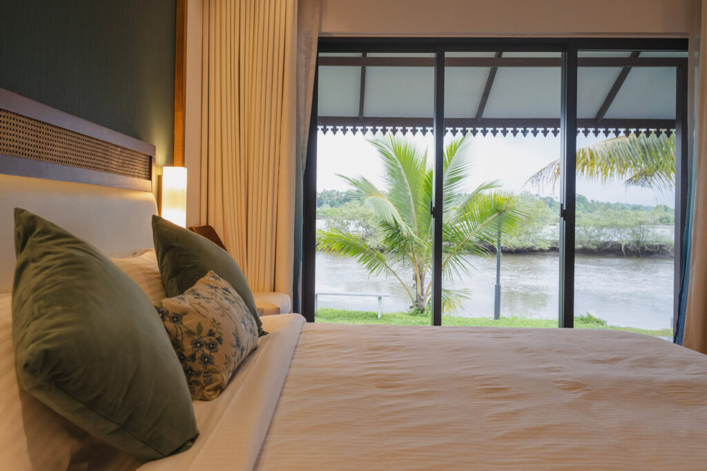 Bedroom in Pavizhamalli villa at Giby Farm with glass doors opening to the palms